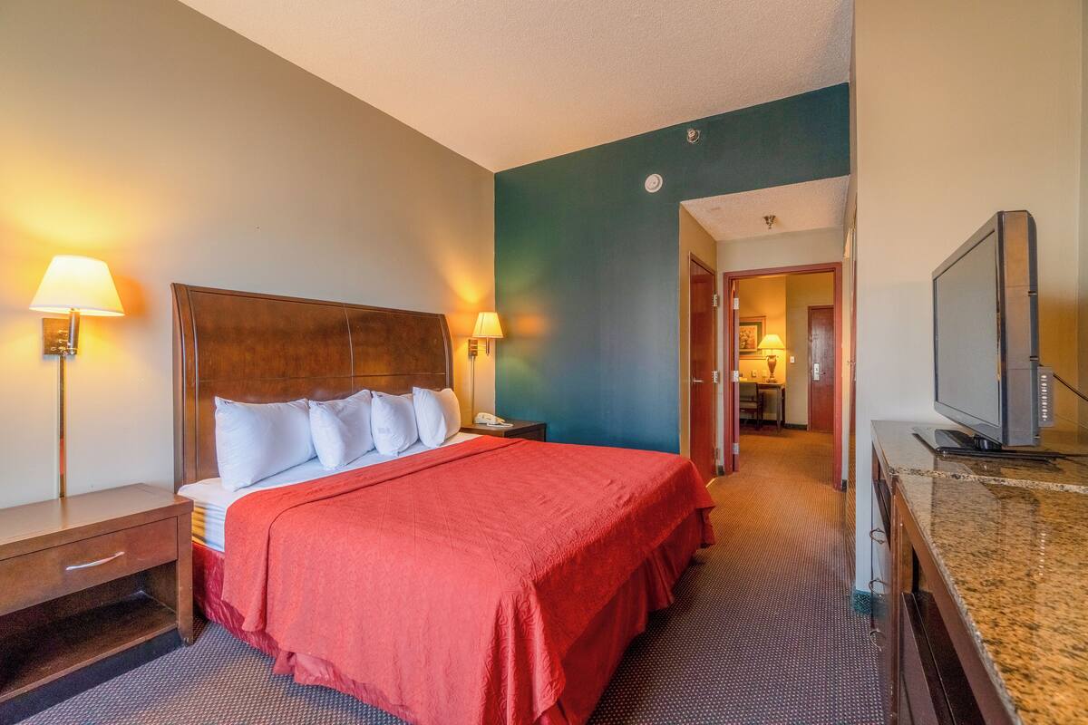 A hotel room with a large bed, two bedside lamps, a television, and a hallway leading to a bathroom.