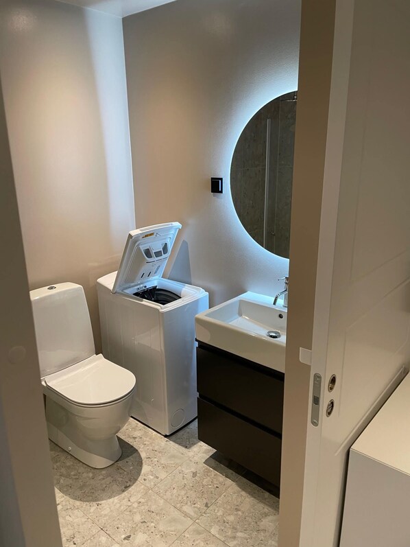 A compact bathroom with a toilet, washing machine, and sink.