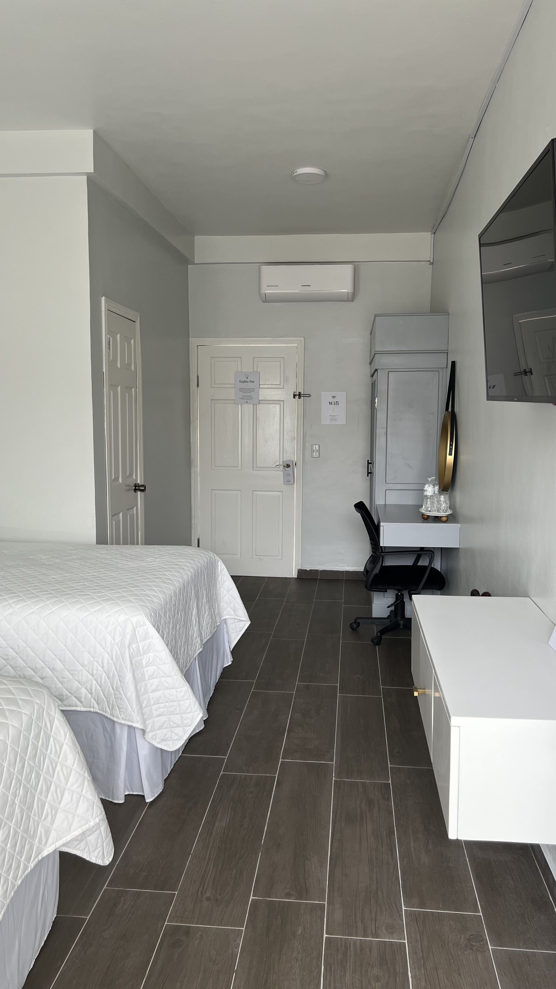 A hotel room with two beds, a desk, a chair, a white wardrobe, and an air conditioning unit.