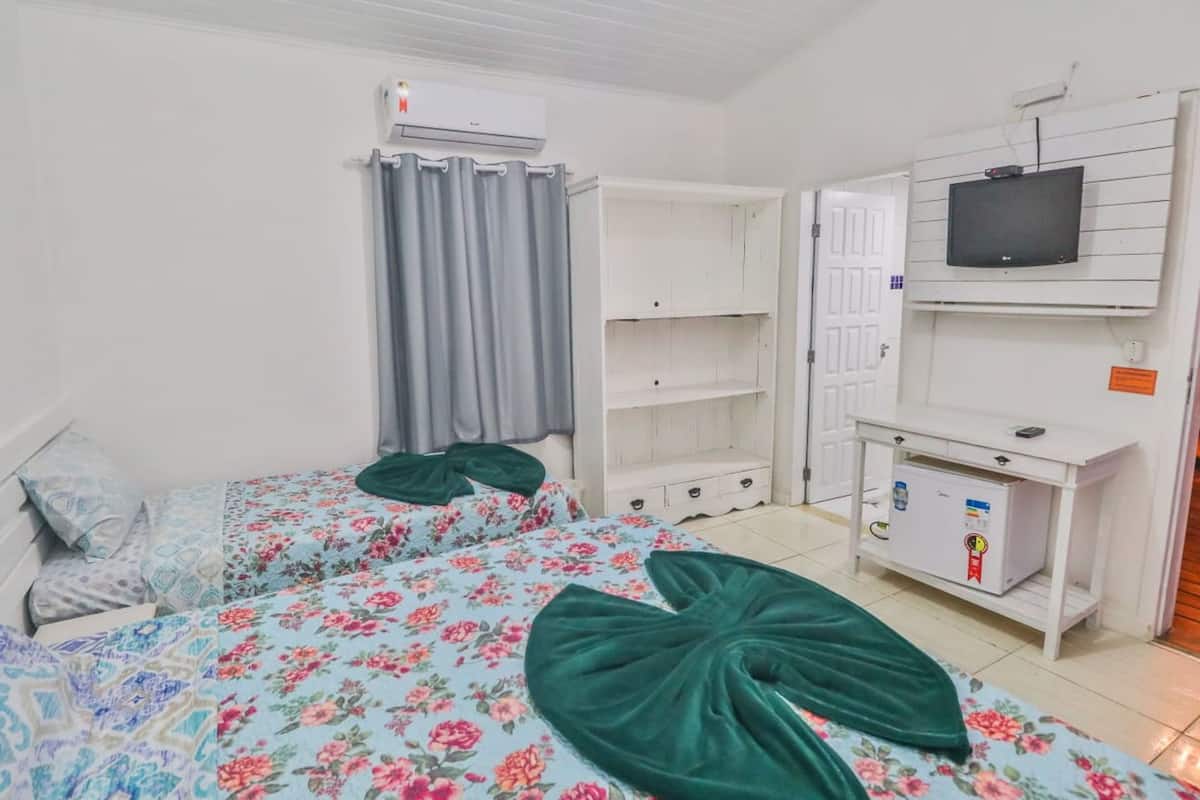 A bedroom with two beds, a TV, a wardrobe, and a small desk.