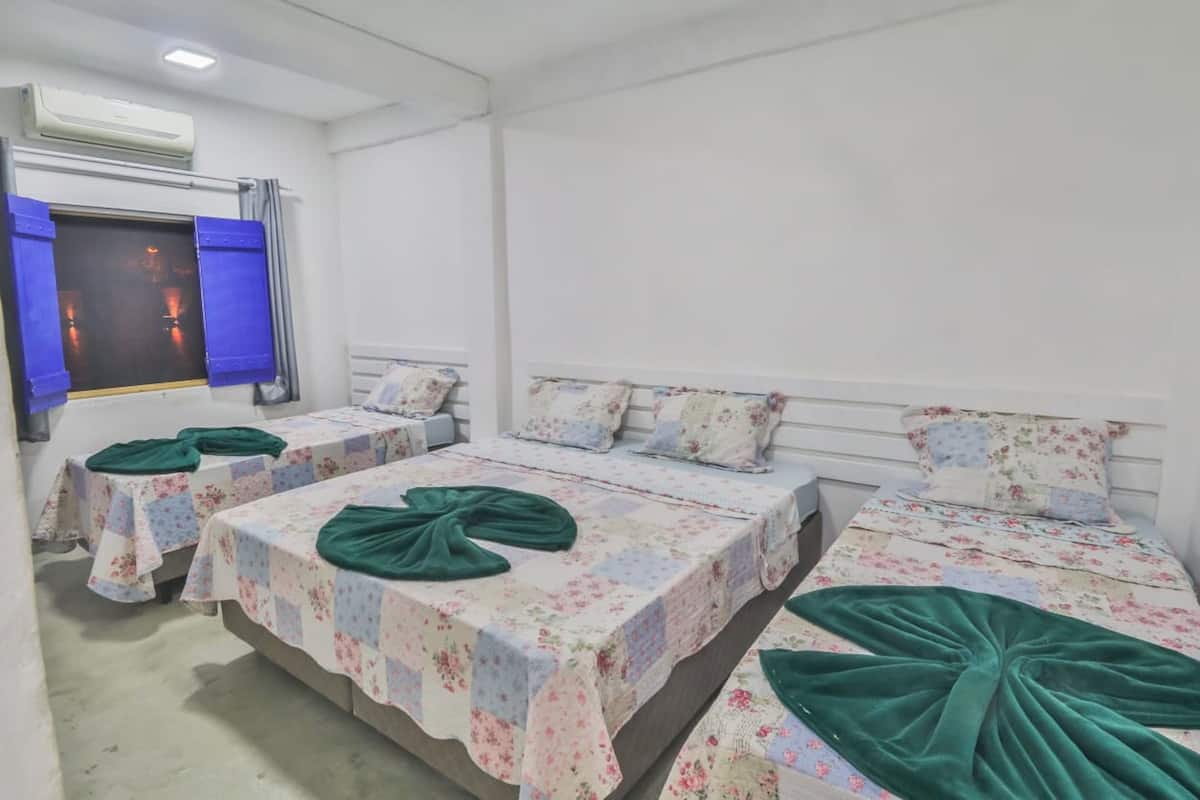 A hotel room with three single beds, each with a floral bedspread and green throw pillows.