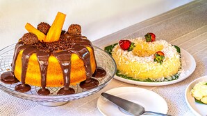 A dessert with chocolate drizzle and a fruit-topped cake on a table. - La Gloria House (Ilhabela)