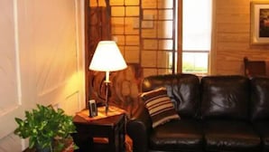 A cozy living room with a leather sofa, a lamp, and a decorative wall panel. - 1831 House in Historic Old Towne Petersburg, VA (Petersburg)