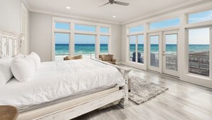 Een slaapkamer met een groot bed, een plafondventilator en uitzicht op de oceaan door grote ramen.