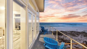 Een balkon met uitzicht op het strand en de oceaan tijdens zonsondergang.