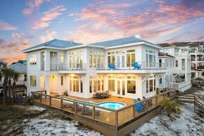Une maison à deux étages située en bord de mer, dotée d’une piscine, d’une terrasse et de plusieurs balcons.