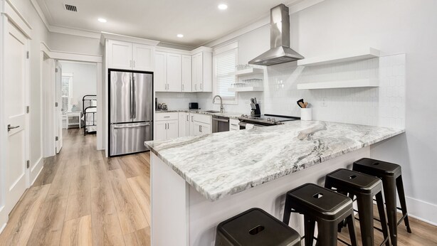 A modern kitchen with white cabinetry, a stainless steel refrigerator, a marble countertop, and a built-in stove.