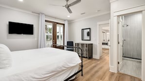 A modern bedroom with a bed, a ceiling fan, a TV, and a view of the kitchen and bathroom.