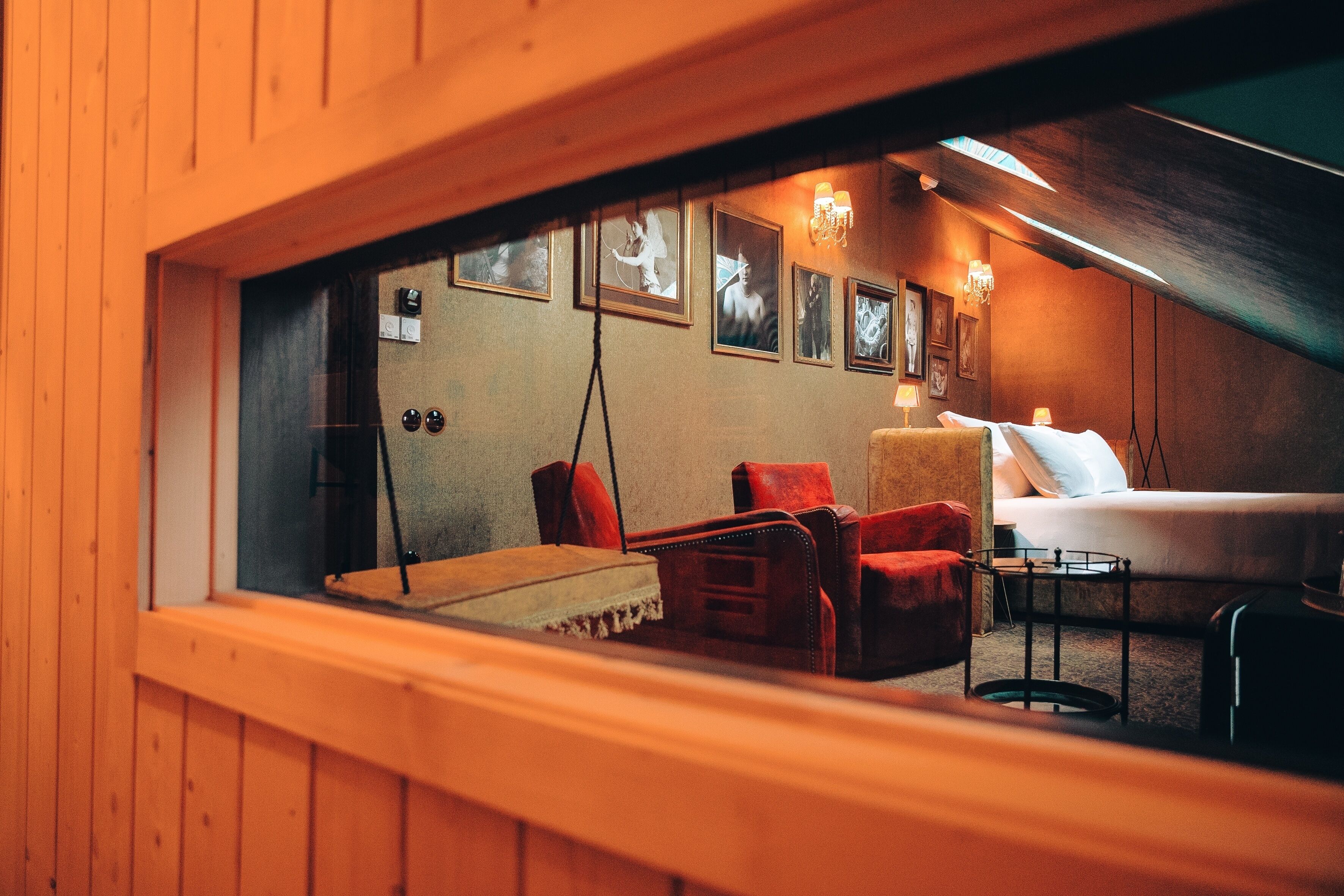 A cozy room with a bed, a red armchair, a small table, and a window overlooking a balcony.