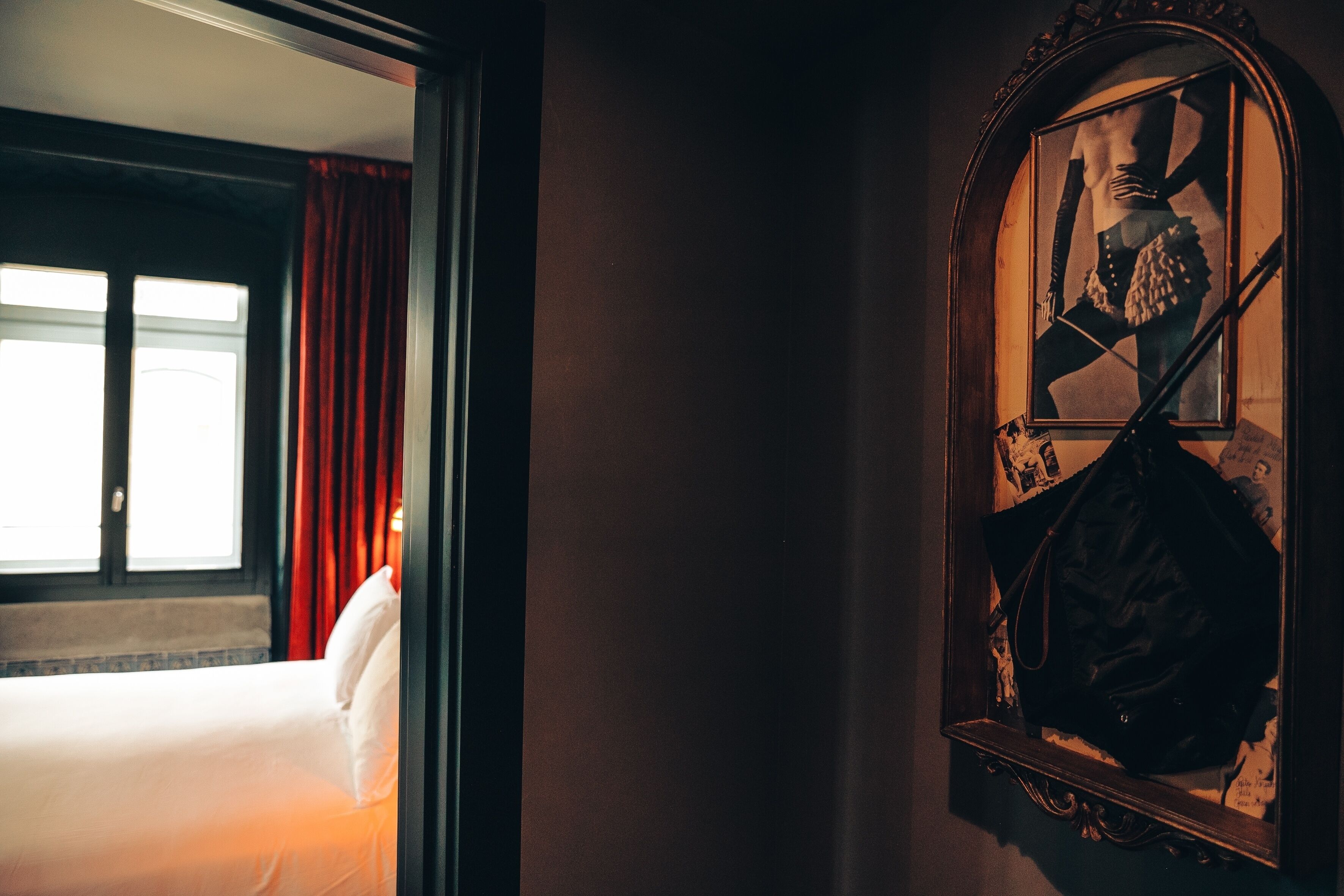 Una habitación de hotel con cama, espejo y ventana con cortinas rojas.