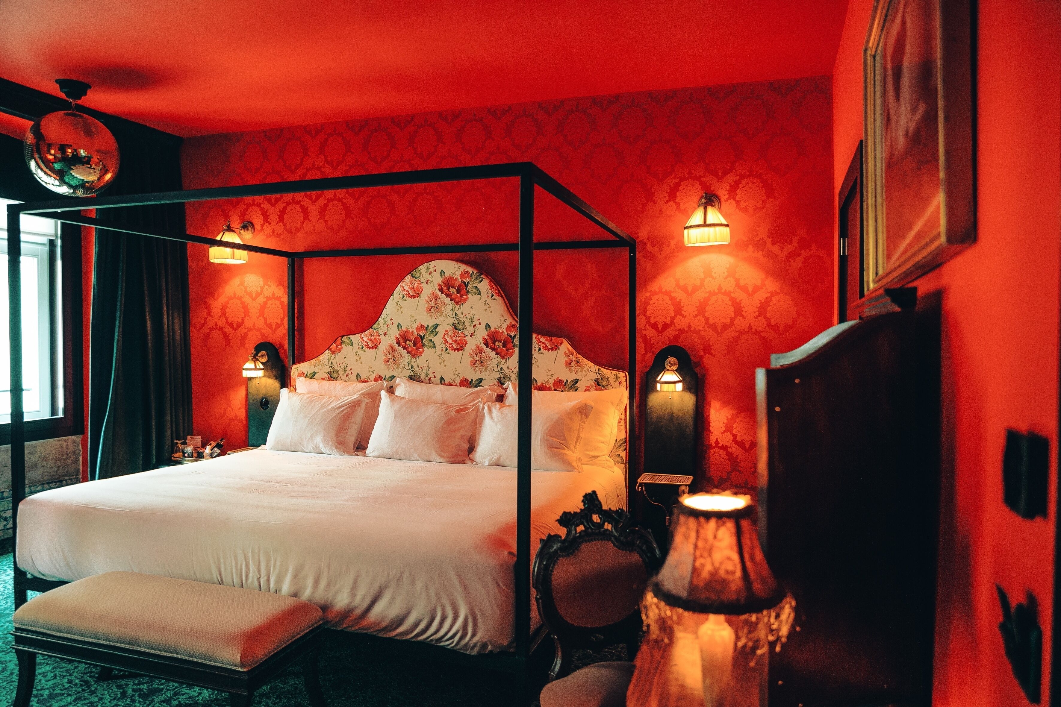Un lit à baldaquin avec une tête de lit à motifs floraux, des lampes de chevet et un banc.