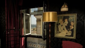 A room with a large window, a red chair, a lamp, and a framed painting on the wall. - Pensão Amor Madam’s Lodge (Lisbon)