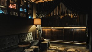 A dimly lit lounge area with a plush sofa, a round table, and a lamp. - Pensão Amor Madam’s Lodge (Lisbon)