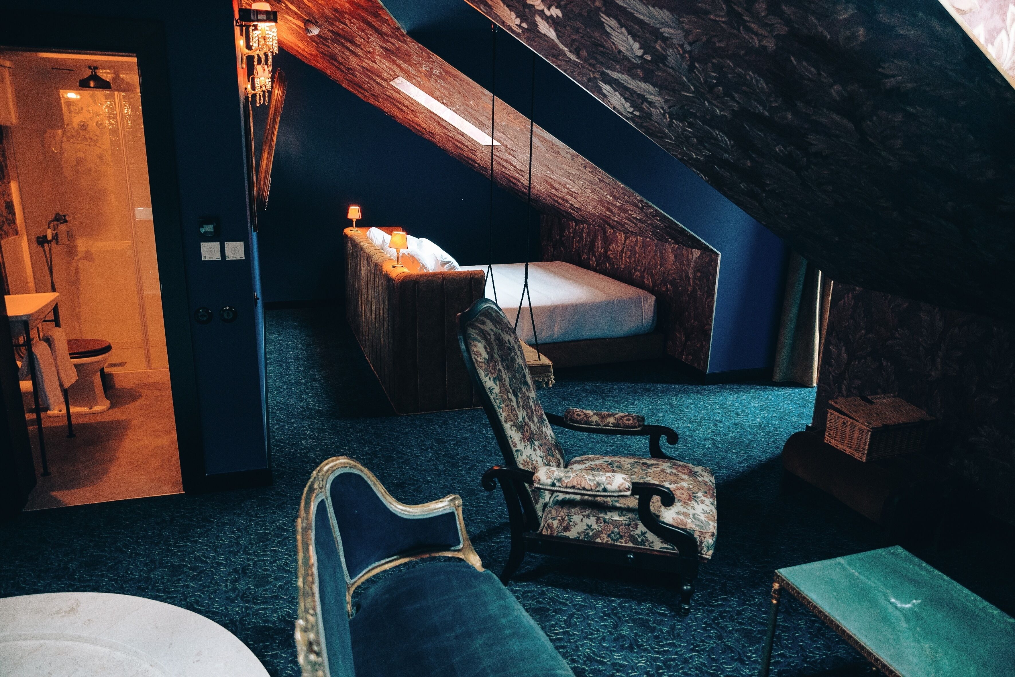 Un dormitorio acogedor en el ático con techo inclinado, una cama, una silla y una mesita.