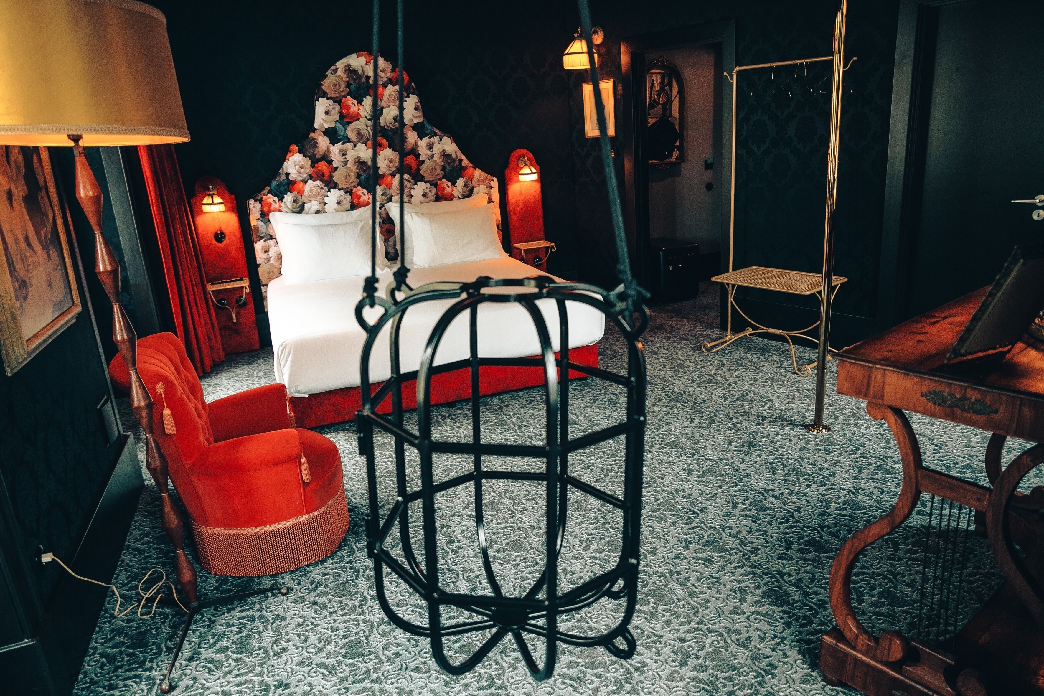 A room with a bed, a red chair, a hanging chair, and a small table.