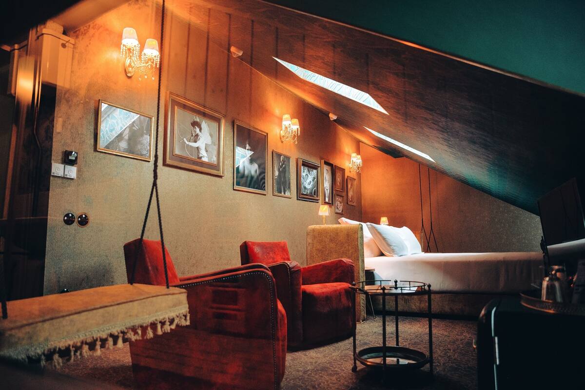Una habitación de hotel acogedora con cama, sillones rojos, una mesita y luces fijadas a la pared.
