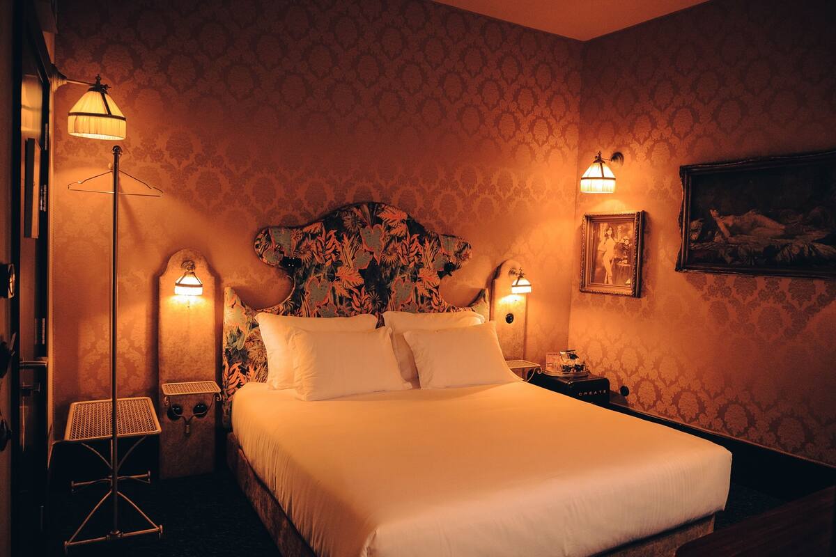 Habitación de hotel con una cama grande, dos mesitas de noche, una lámpara de pie y un cuadro colgado en la pared.