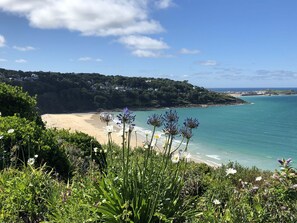 A coastal landscape with a sandy beach, a clear blue sky, and lush greenery. - 4 Pentowan Court (St Ives)