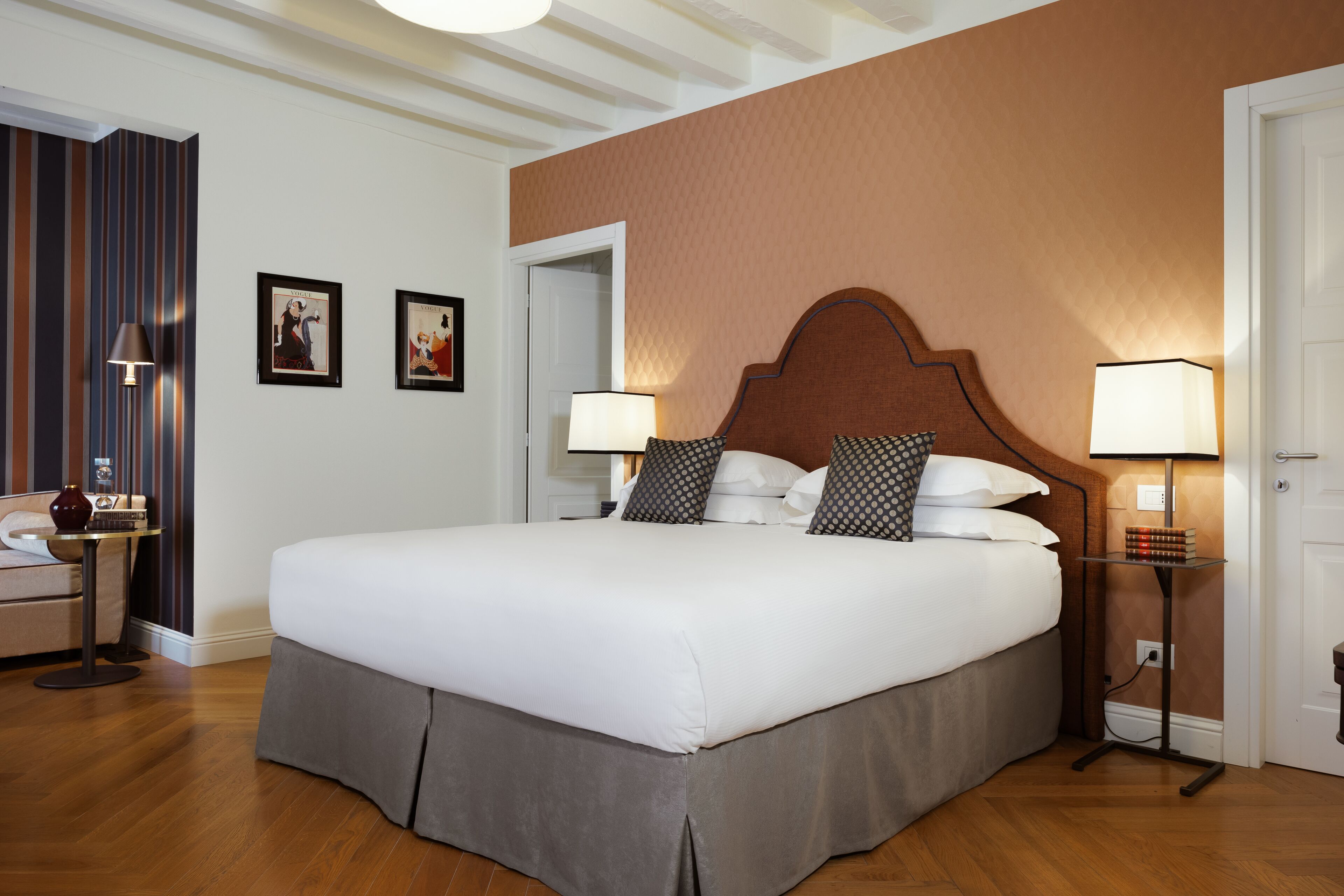 Una cama grande con cabecera de madera, dos lámparas de noche y una mesita con un florero.