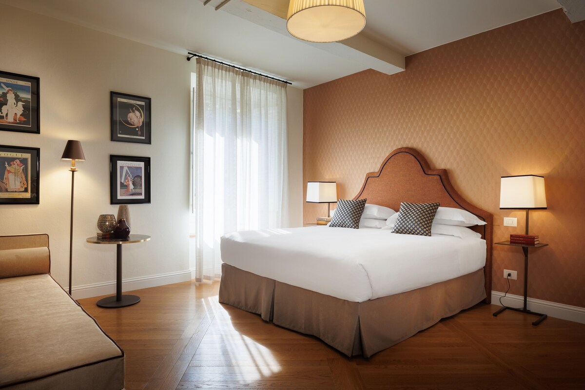 A large bed with a wooden headboard, two bedside lamps, and a bedside table with a lamp and a vase.