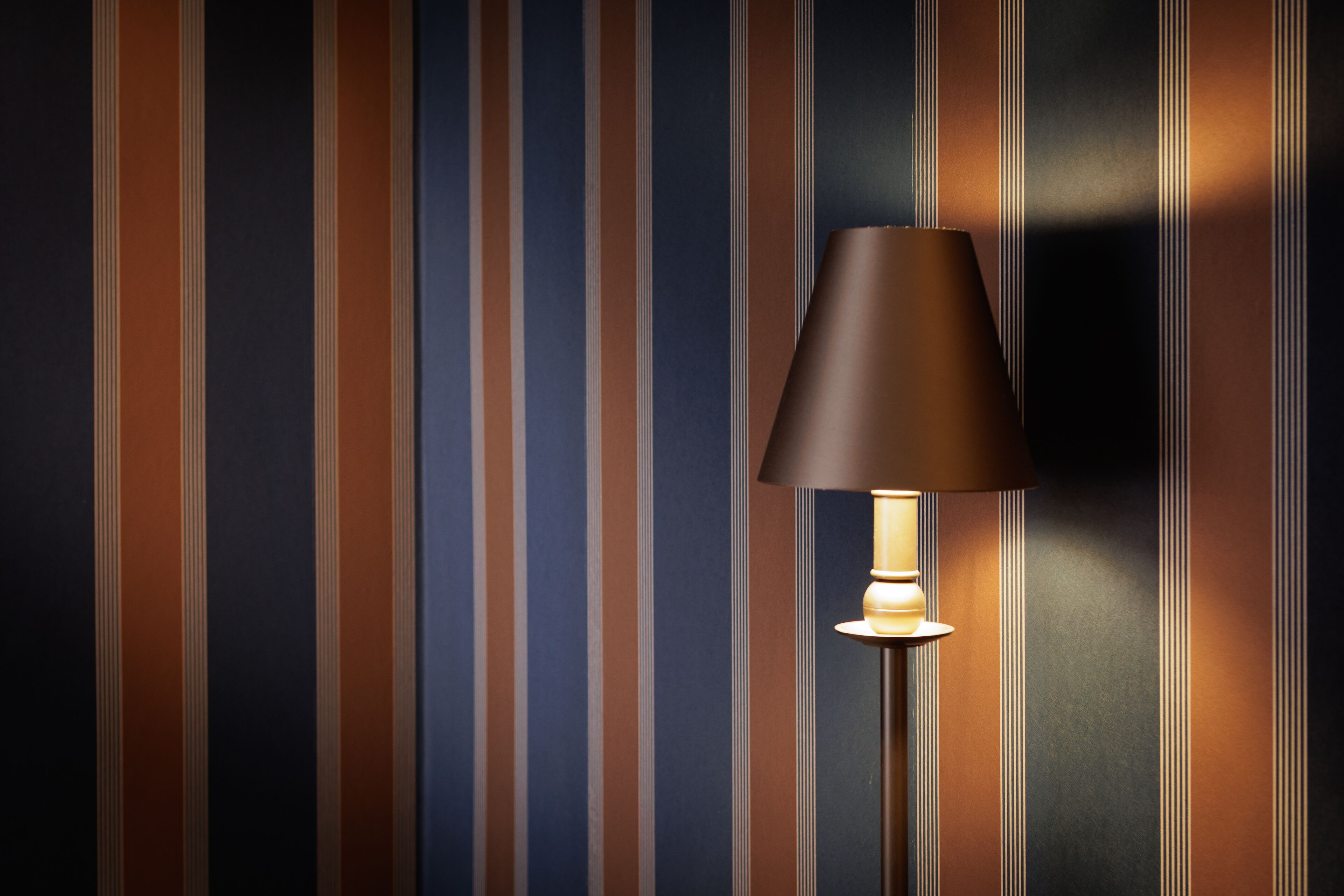 A floor lamp with a dark shade against a striped wall.