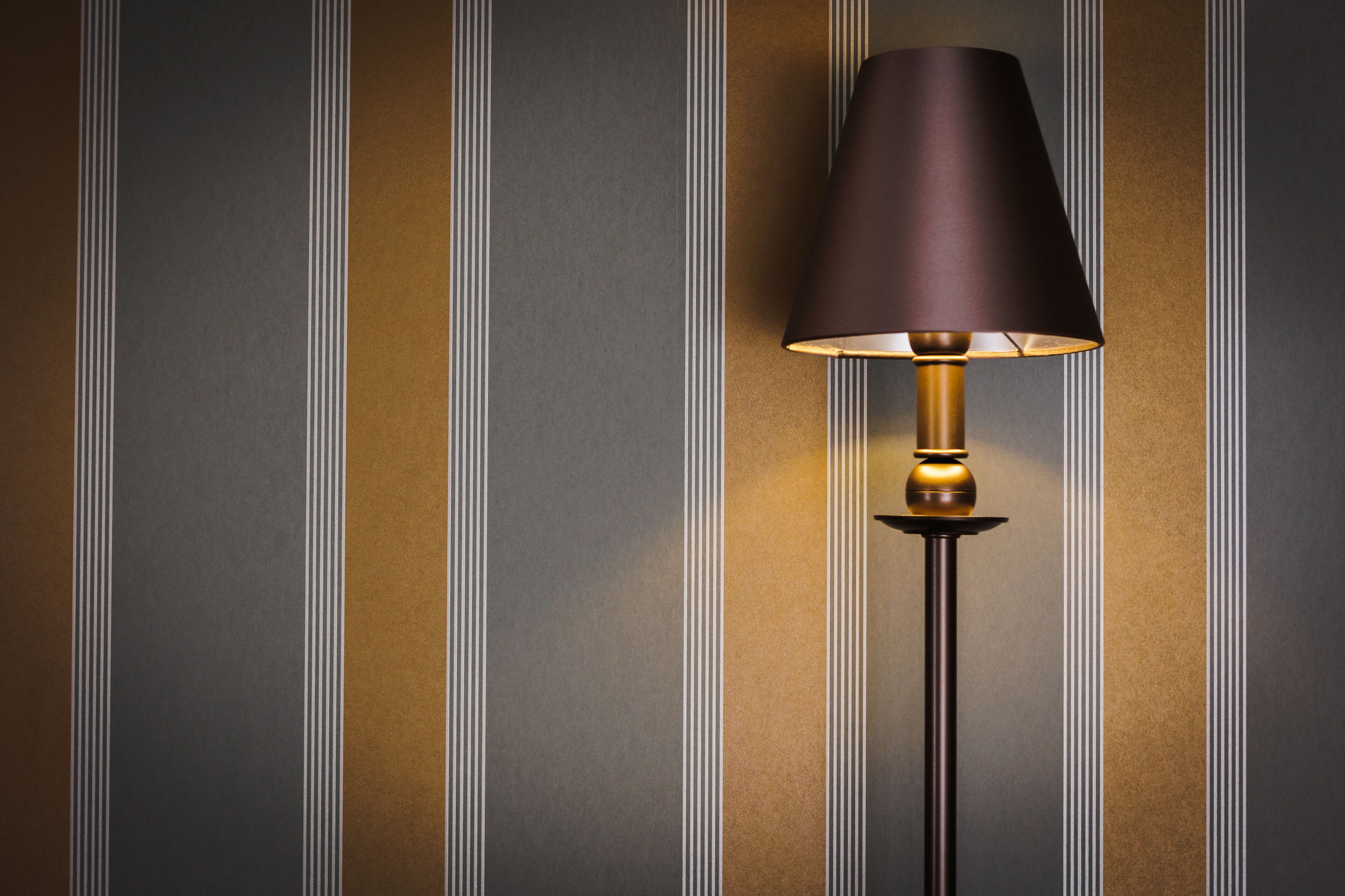 A floor lamp with a dark shade and a gold base against a striped wall.