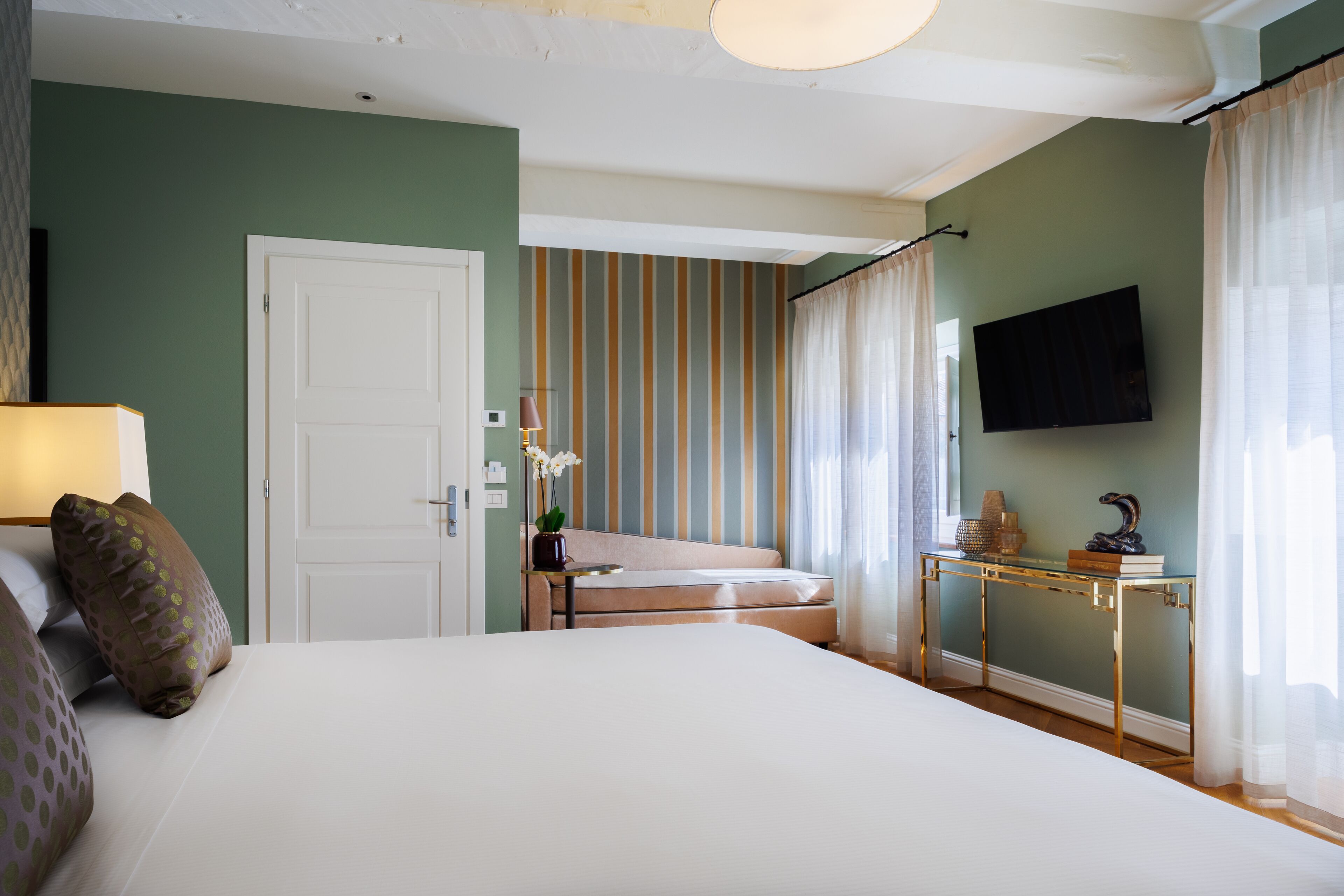 A bedroom with a bed, a bedside table, a lamp, a television, and a window with curtains.