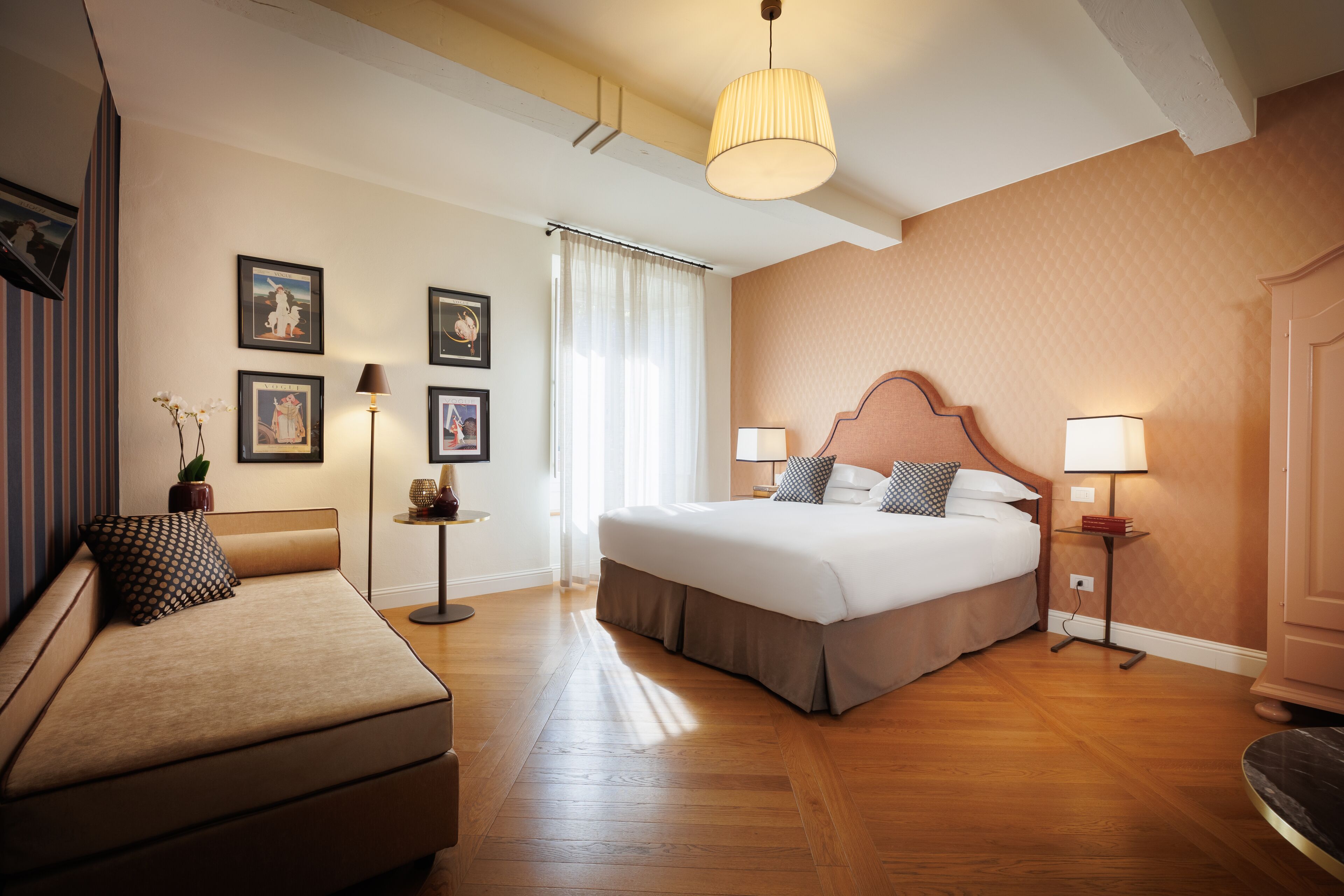 A hotel room with a bed, a sofa, a standing lamp, and framed pictures on the wall.