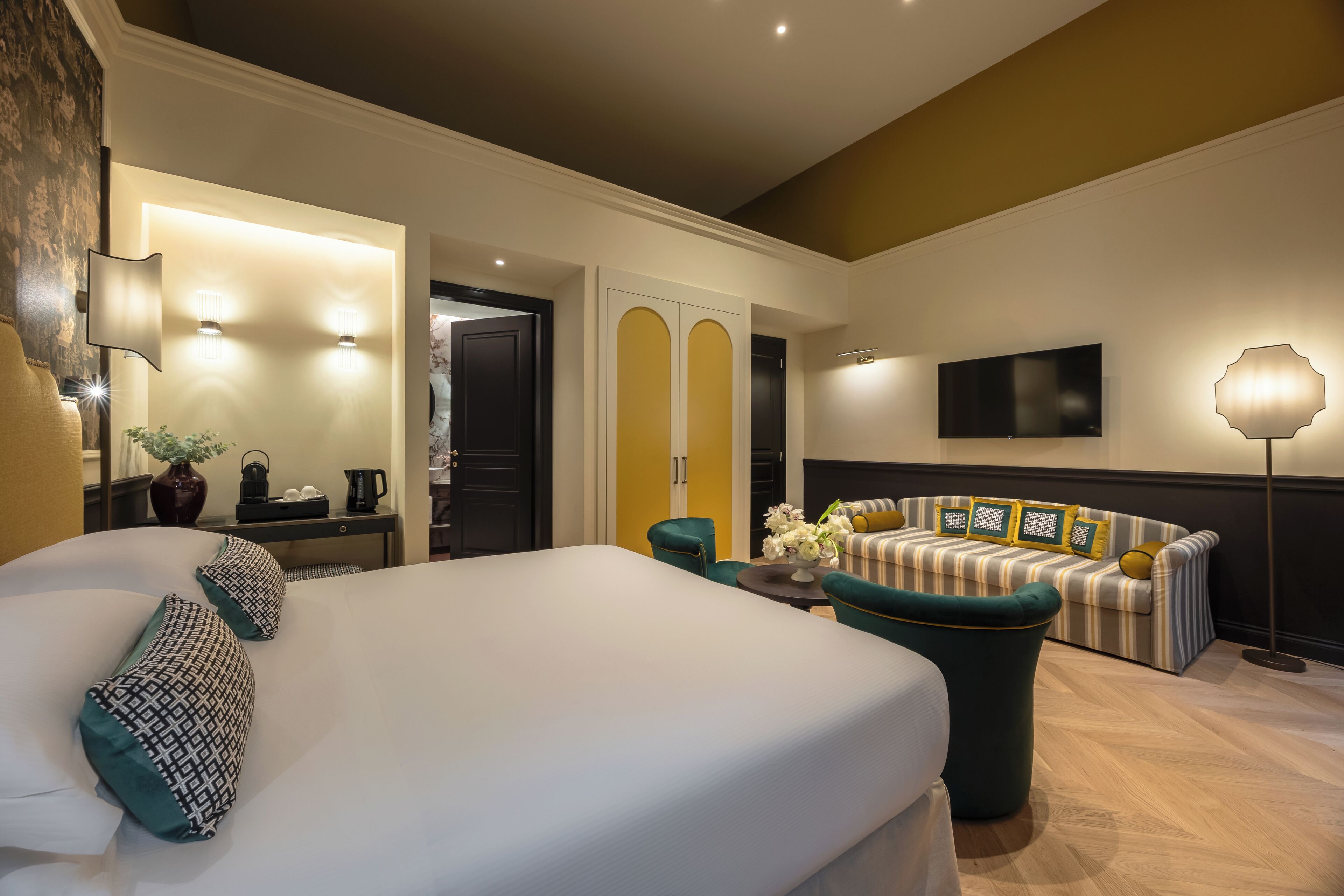 A hotel room with a large bed, a sofa, a TV, and a lamp.