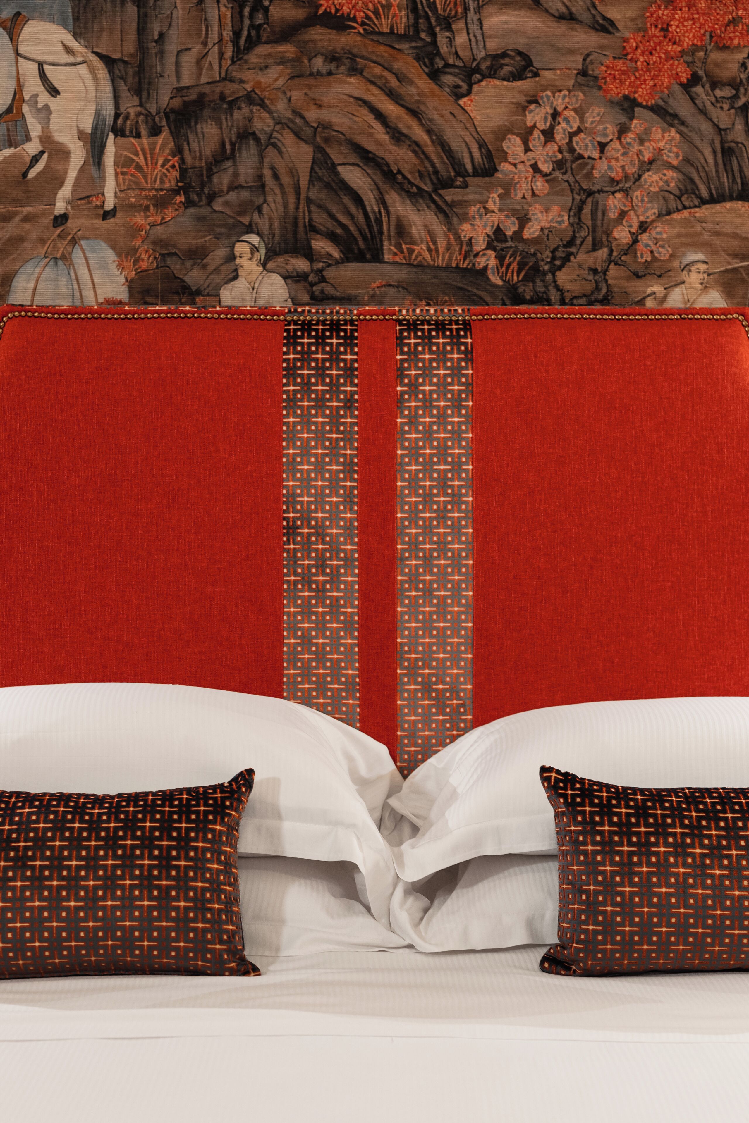 A bed with a red headboard, two pillows, and a patterned fabric strip.