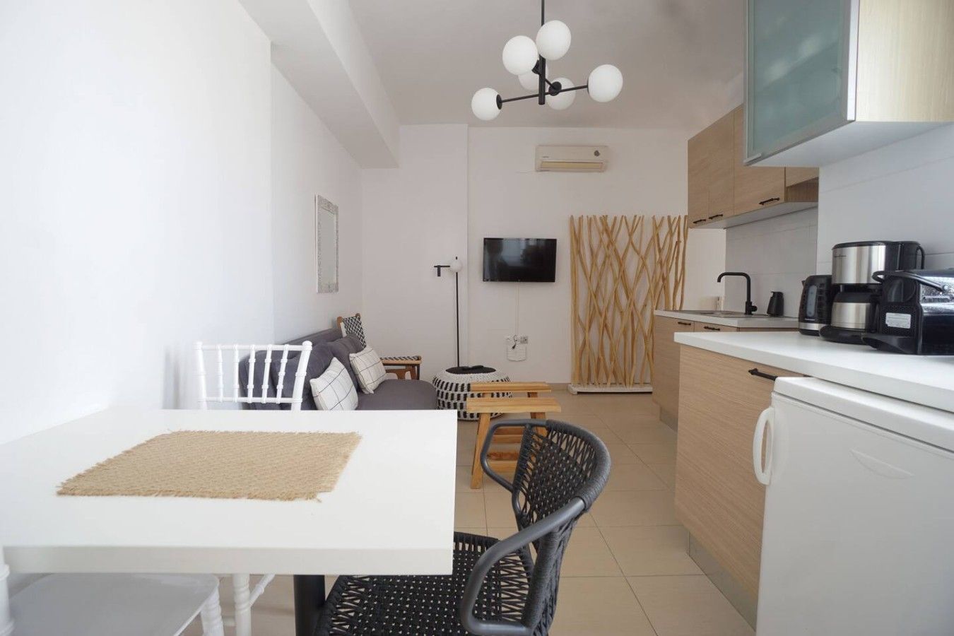 A modern kitchen with a dining area, white cabinetry, and a flat-screen TV.