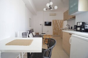 A modern kitchen with a dining area, white cabinetry, and a flat-screen TV.