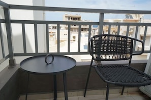 A balcony with a round table and a wicker chair, overlooking a residential area.