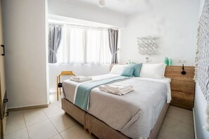 A modern bedroom with a large bed, a wooden nightstand, a chair, and a wall-mounted lamp. - Urban Beach (1D) (Ρέθυμνο)
