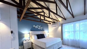 A bedroom with a bed, bedside tables, a rug, a wall art piece, and a window with curtains. - Starfish Room — Coastal Luxury & Romantic Comfort at Mar Bella (Rehoboth Beach)