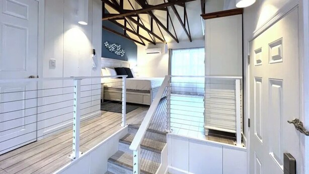 A staircase with white railings, a wooden floor, and a ceiling with exposed beams. - Starfish Room — Coastal Luxury & Romantic Comfort at Mar Bella (Rehoboth Beach)