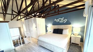 A bedroom with a bed, bedside tables, a wardrobe, and a ceiling with exposed beams. - Starfish Room — Coastal Luxury & Romantic Comfort at Mar Bella (Rehoboth Beach)