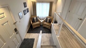 A corner room with a sofa set, a window with curtains, a door, and a staircase. - Starfish Room — Coastal Luxury & Romantic Comfort at Mar Bella (Rehoboth Beach)