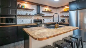 A modern kitchen with dark cabinets, a wooden island, stainless steel appliances, and a herringbone-patterned backsplash. - Upscale Helen Cabin on 1 Wooded Acre (White County)