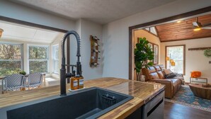 A modern kitchen with a large sink, wooden countertop, and a view into the living area with a leather couch and a plant. - Upscale Helen Cabin on 1 Wooded Acre (White County)