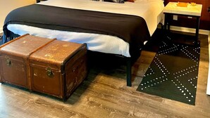 A modern bedroom with a wooden headboard, a large bed with a black and white bedspread, multiple pillows, a wooden chest of drawers, a nightstand, and a wall art piece. - Upscale Helen Cabin on 1 Wooded Acre (White County)