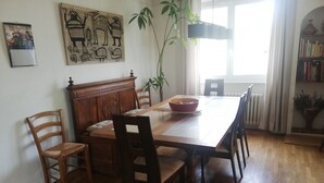 Een eethoek met een houten tafel, stoelen, een schaal, een plant en een radiator.