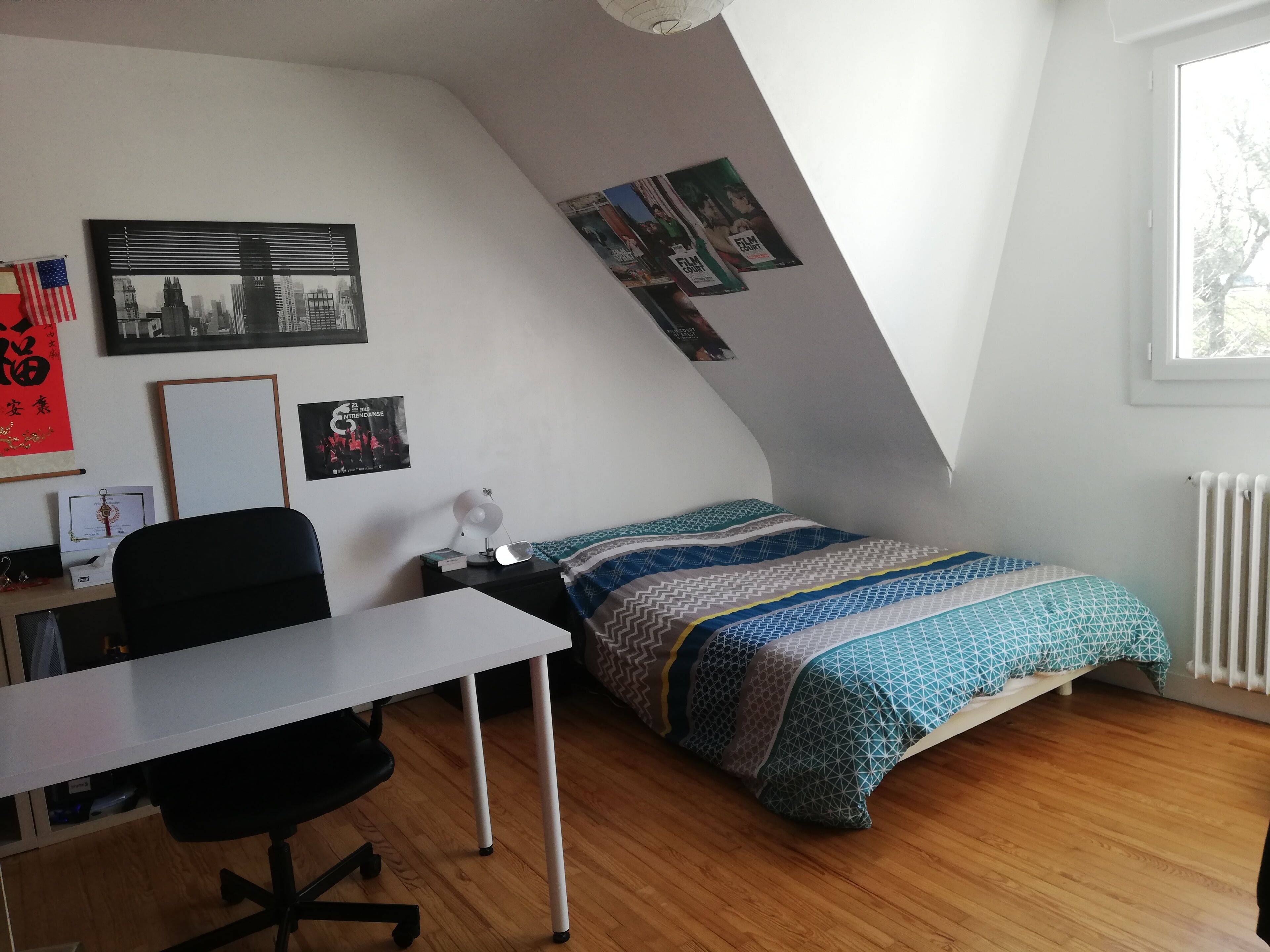 A dorm-style room with a desk, chair, bed, and posters on the wall.