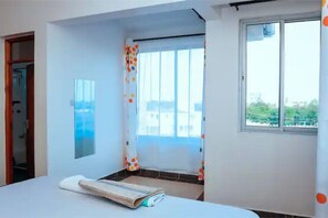 Quarto com cama, janela, porta e vista para o verde lá fora.