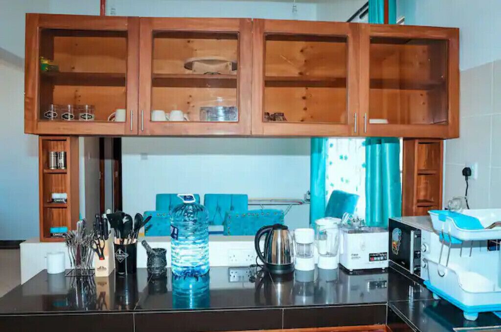A kitchen with wooden cabinets, a countertop with various kitchen items, and a blue sofa in the background.