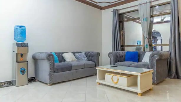 A living room with two grey sofas, a coffee table, and a water dispenser. - Divine apartments (Mombasa)