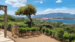 Une vue pittoresque d’une zone côtière, avec une pergola en bois, un mur de pierre et un arbre.