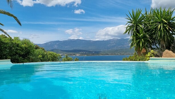 Une piscine d’un bleu éclatant, avec une vue sur les montagnes et un plan d’eau en arrière-plan.