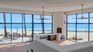 A room with large windows overlooking a beach, a ceiling fan, and a bed.