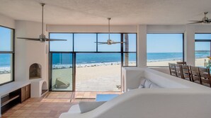 A spacious living area with large windows overlooking a beach, a ceiling fan, and a built-in fireplace.